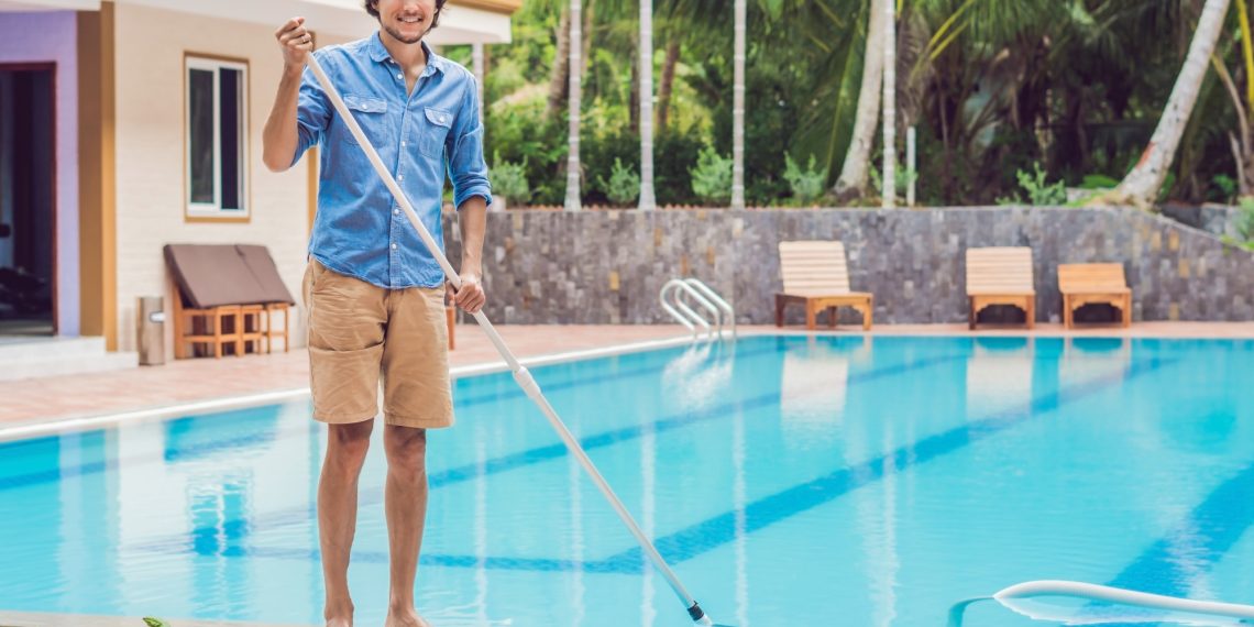Cleaner of the swimming pool . Man in a blue shirt with cleaning equipment for swimming pools, sunny.